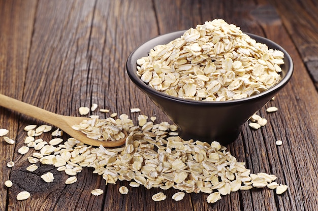 Farina d'avena o fiocchi d'avena in una ciotola nera e vicino al tavolo di legno scuro