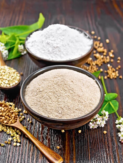 Farina di grano saraceno da cereali marroni e verdi in due ciotole, cucchiai con semole, fiori e foglie sullo sfondo di una tavola di legno