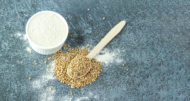 Farina di grano saraceno in una ciotola bianca e cucchiaio di legno, grano saraceno verde crudo su fondo di cemento