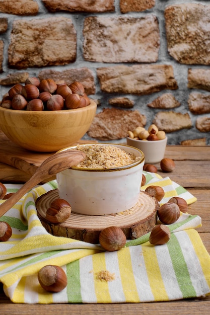 Farina di nocciole macinata organica cruda in una ciotola con noci intere su fondo di legno rustico Farina di noci alternativa