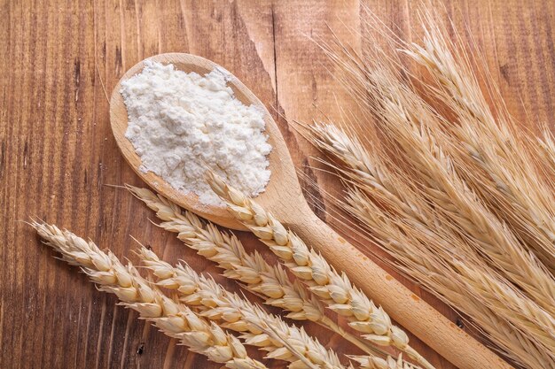 Farina in cucchiaio di legno e spighe di grano sul concetto di cibo e bevande a bordo vintage