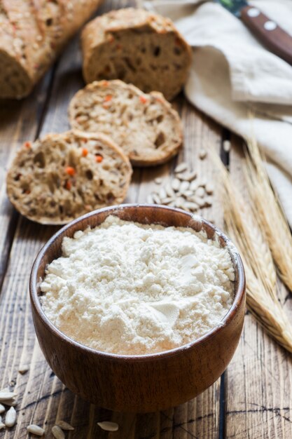 Farina in una ciotola di legno e pezzi di pane di grano su un tavolo di legno