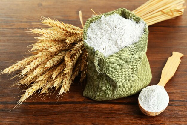 Farina intera in sacchetto di tela da imballaggio con spighe di grano sul primo piano della tavola di legno