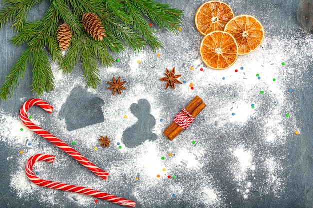 Farina silhouette di biscotti sul buio tra i rami degli alberi di Natale, coni, anice stellato, cannella e bastoncino di zucchero.