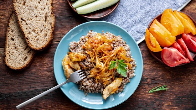 Farinata di grano saraceno con carne, cipolle e carote su un fondo di legno. Con verdure fresche, cetrioli e pomodori.