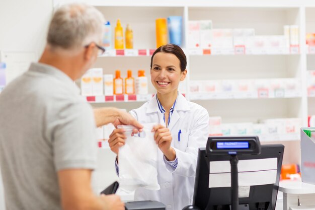 farmacie assistenza sanitaria e persone concetto farmacista donna che dà al cliente maschio anziano il suo acquisto in borsa in farmacia