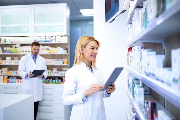 Farmacista biondo femminile che controlla l'inventario della medicina alla farmacia.