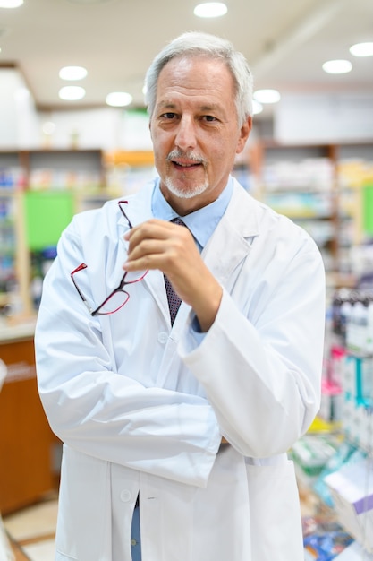 Farmacista senior nel suo negozio sorridendo mentre si tiene gli occhiali