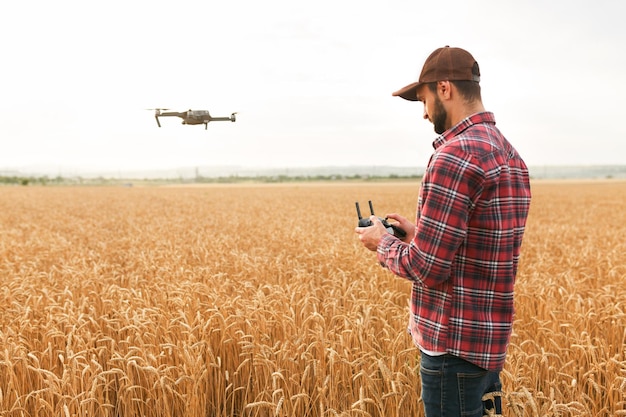 Farmer holds remote controller with his hands while quadcopter is flying on background Drone hovers behind the agronomist in wheat field Agricultural new technologies and innovations Back view