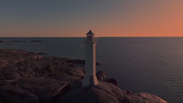 Faro di navigazione marina su un promontorio di granito illuminato dal sole al tramonto Seascape