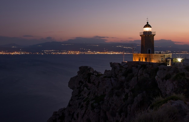 Faro di paesaggio notturno sulla montagna rocciosa sullo sfondo della città di notte in Grecia