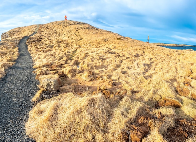 Faro di Stykkisholmur sulla collina con prato giallo sotto il cielo blu nuvoloso in Islanda