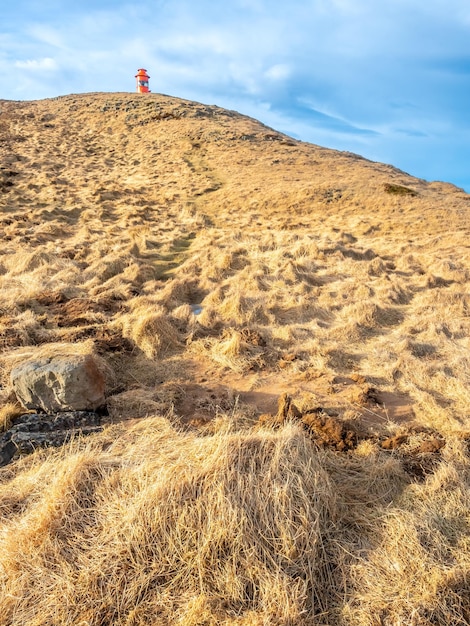 Faro di Stykkisholmur sulla collina con prato giallo sotto il cielo blu nuvoloso in Islanda