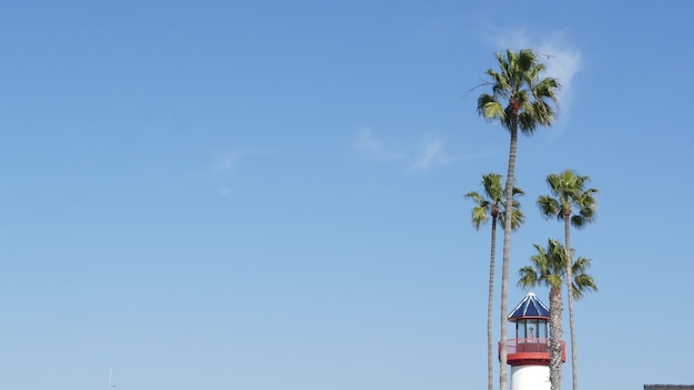 Faro retrò, palme tropicali e cielo blu. Faro antiquato vintage rosso e bianco. Villaggio di pescatori di lungomare vicino al porto del mare dell'oceano. Molo o porto marittimo, estate soleggiata in California USA.