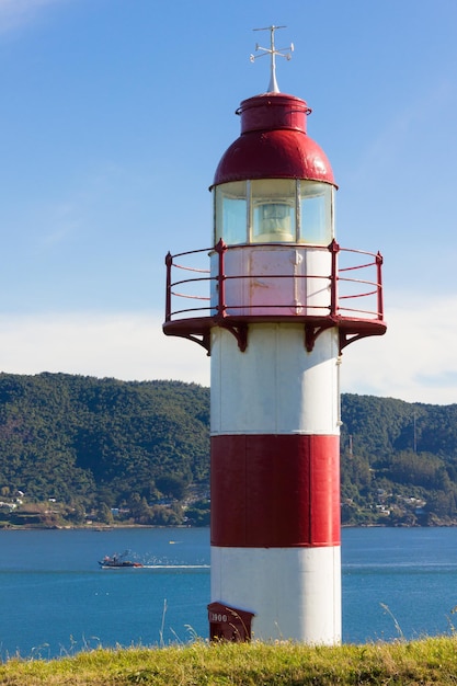 Faro rosso e bianco con la barca da pesca che si dirige al molo in giornata di sole al Forte di Niebla in Cile