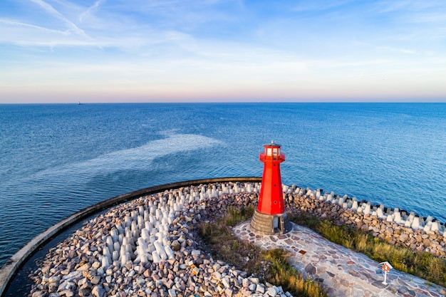 Faro rosso sul porto roccioso al tramonto