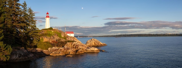 Faro su una costa rocciosa durante un vivace tramonto nuvoloso