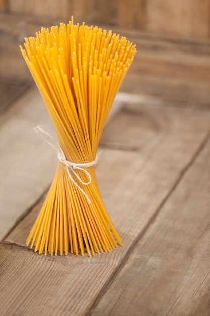 Fascio di spaghetti crudi legati con corda su fondo di legno