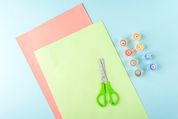 Fase uno di come realizzare una farfalla di carta origami con carta verde, forbici su sfondo blu