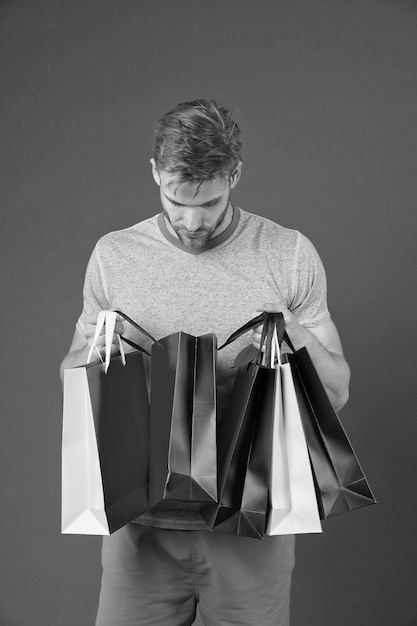 Fashion shopper look in paperbag Uomo con borse della spesa su sfondo viola Macho con sacchetti di carta colorati Preparazione e celebrazione delle feste Shopping o saldi e cyber monday
