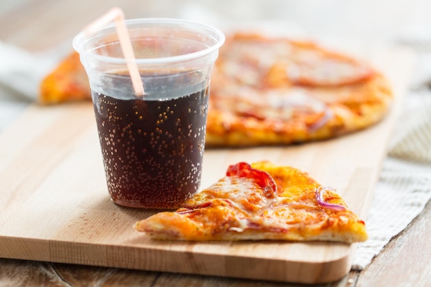 fast food, cucina italiana e concetto di mangiare - primo piano di pizza con una tazza di bevanda coca cola sul tavolo di legno