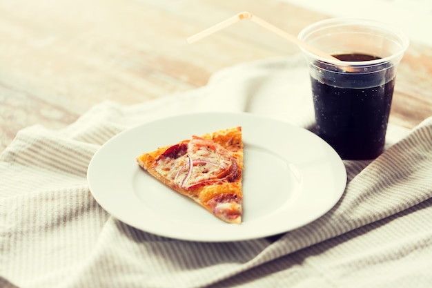 fast food, cucina italiana e concetto di mangiare - primo piano di una fetta di pizza con una tazza di bevanda coca cola su un tavolo di legno