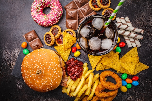 Fast food e zucchero. Burger, dolci, patatine, cioccolato, ciambelle, soda, vista dall&#39;alto.