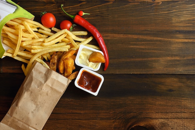 Fast food: patatine fritte con salsa e ingredienti alimentari sul tavolo di legno scuro