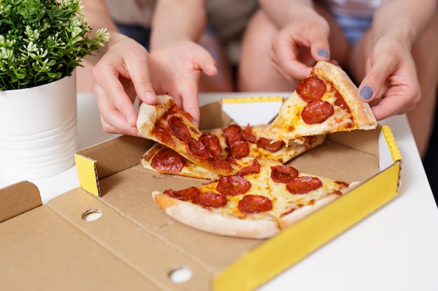 Fast food - primo piano di mani femminili che prendono fette di pizza ai peperoni dalla scatola di cartone