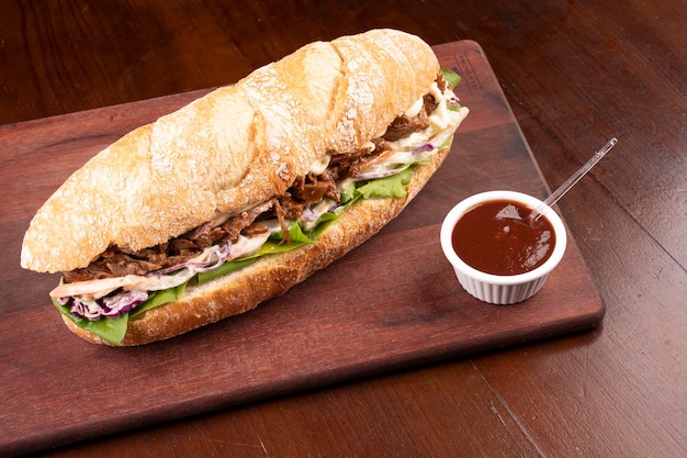 Fast food sandwich di petto di manzo con rucola e insalata di coleslaw su baguette su tavola di legno con salsa barbecue nell'angolo vista dall'alto