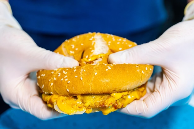 Fast food Vista macro dell'hamburger Mani in guanti di lattice bianchi che tengono hamburger che mostrano formaggio gustoso e cotoletta Primo piano