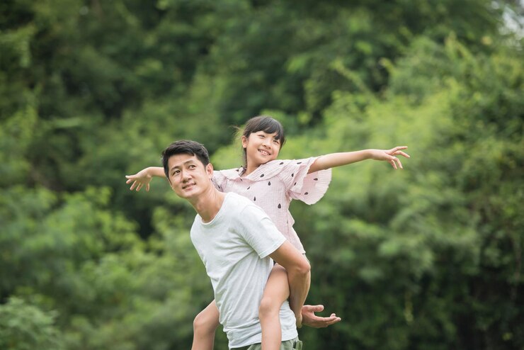 Father carrying daughter on back in the park Happy family concept