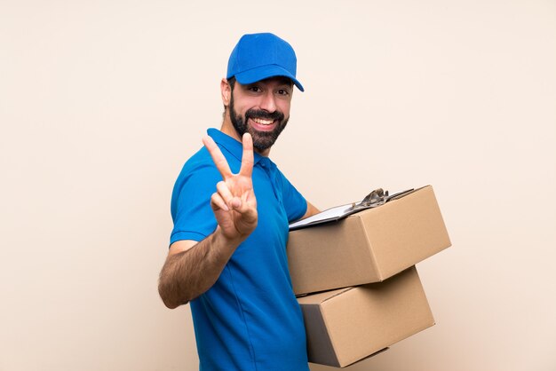 Fattorino con la barba sopra la parete isolata che sorride e che mostra il segno di vittoria