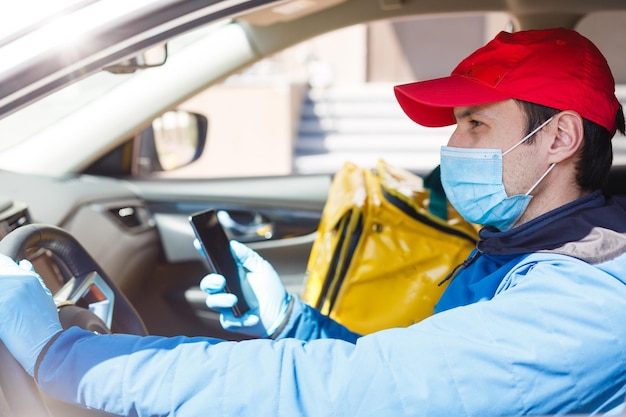 fattorino del cibo con maschera protettiva e guanti con uno zaino termico vicino a un'auto durante il periodo di quarantena