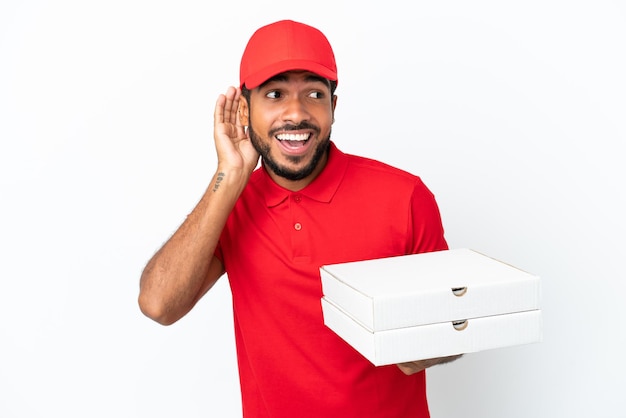 Fattorino della pizza che preleva scatole per pizza isolate su sfondo bianco ascoltando qualcosa mettendo la mano sull'orecchio