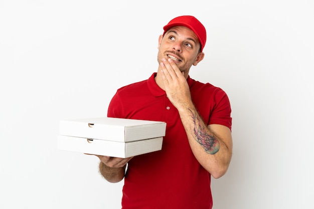 Fattorino della pizza con l'uniforme da lavoro che prende le scatole della pizza sopra la parete bianca isolata che guarda in su mentre sorride
