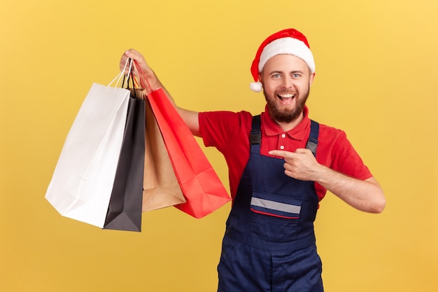 Fattorino in cappello di babbo natale e uniforme che punta alle borse della spesa in mano