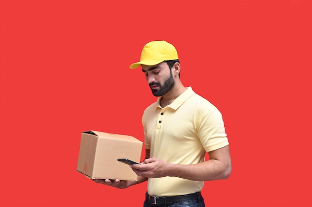 fattorino in maglietta gialla che usa il cellulare e tiene in mano una scatola di imballaggio modello indiano pakistano