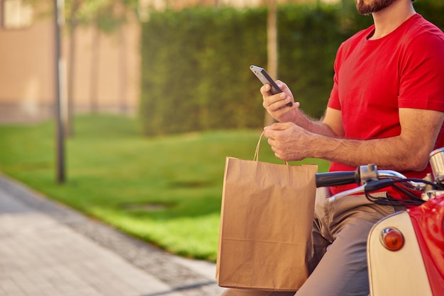 Fattorino in uniforme che tiene pacchetto di carta e smartphone