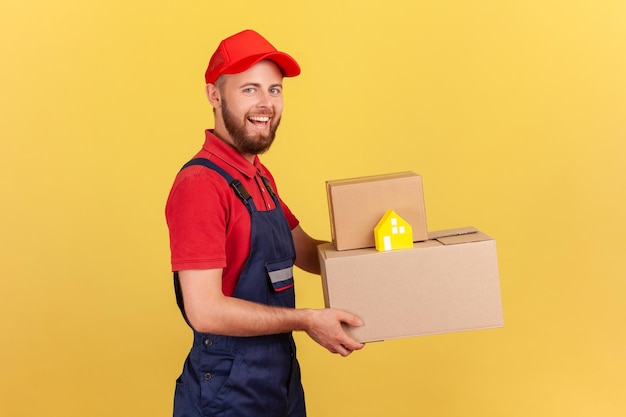 Fattorino in uniforme e cappuccio rosso che tiene scatole di cartone e consegna porta a porta di casa di carta