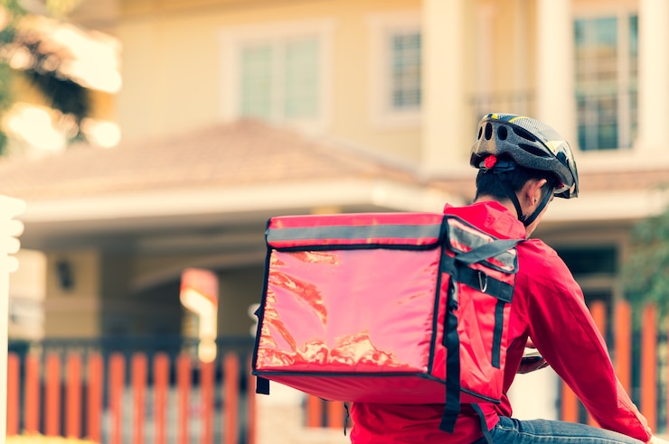Foto fattorino in uniforme rossa in bicicletta per consegnare i prodotti ai clienti a casa.