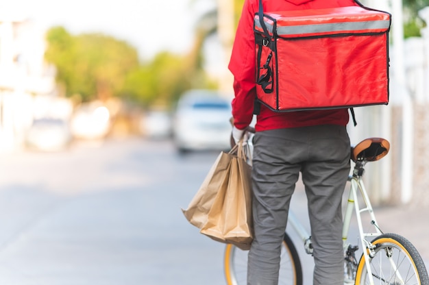 Fattorino in uniforme rossa in bicicletta per consegnare i prodotti ai clienti a casa.