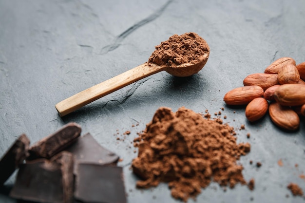 Fave di cacao organiche, polvere di cacao in un cucchiaio di legno e cioccolato su uno sfondo di pietra nera