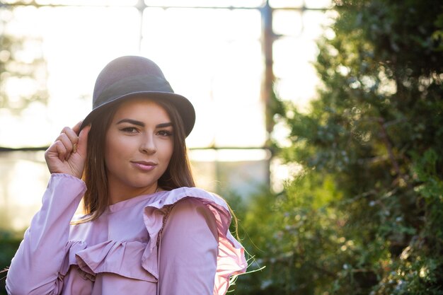 Favolosa ragazza abbronzata che indossa camicetta e cappello alla moda, in posa all'aperto con la luce del sole. Spazio vuoto