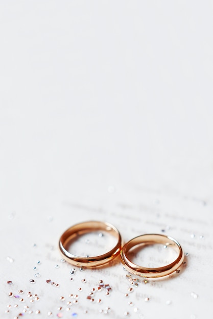 Fedi nuziali dorate su invito di carta con strass brillanti. Dettagli di nozze, simbolo di amore e matrimonio.