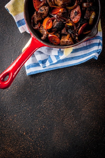 Fegato di manzo arrostito o grigliato con cipolla e carota in padella porzionata, vista tavolo arrugginito scuro