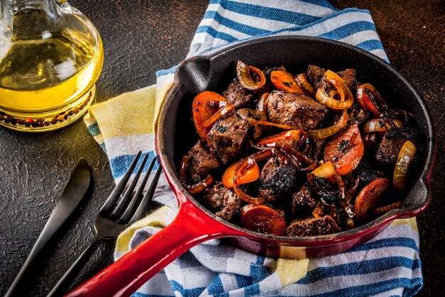 Fegato di manzo arrosto o grigliato con cipolla e carota in padella porzionata, tavolo arrugginito scuro