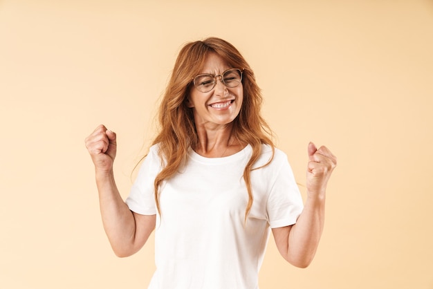 felice adulto maturo bella donna in posa isolato su muro beige fare gesto vincitore.