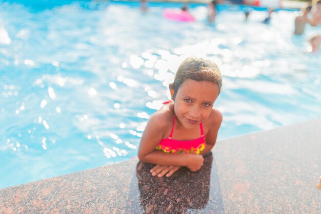 Felice allegra bambina in costume da bagno colorato emerge dalla piscina in una calda giornata estiva di sole