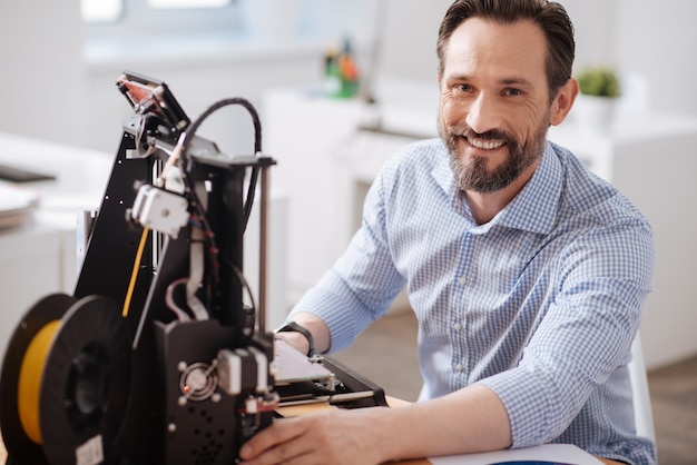 Felice allegro bell'uomo seduto al tavolo e sorridente mentre si gode il suo lavoro con le tecnologie 3d